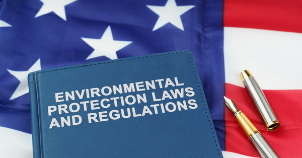 A blue book titled "Environmental Protection Laws and Regulations" sits on a United States flag next to a pen.