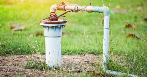A large pipe is coming out of the ground and connects to a smaller pipe that turns to the side. Grass surrounds the pipes.