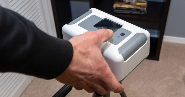 A close-up view shows a technician setting up a white device on a tripod in the interior of a home.