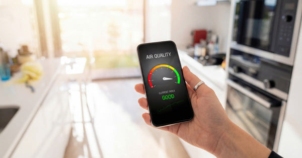 A person stands in a residential kitchen holding a smartphone. The smartphone has a meter and reads, "Air quality good."