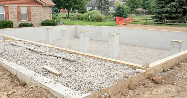 The crawl space of a home is exposed as construction is just beginning for the home. There are three concrete pillars.