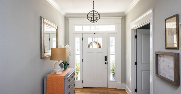 A short hallway with gray walls leads to the white front door of a home. The walls have artwork on them.