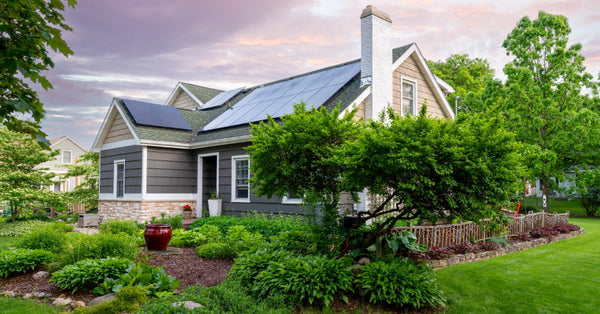 A cute one-story home with dark-colored siding and a landscaped property has solar panels on the roof.