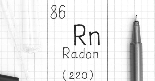 The chemical symbol for Radon (Rn), along with the numbers 86 and 220, is written on paper in a black square.