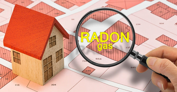A hand holds a magnifying glass that reads "Radon gas" next to a model of a home that sits on a plat map.