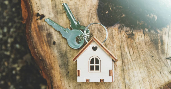 A key ring with a small wooden house charm on it and two silver keys lay on top of an old tree stump.