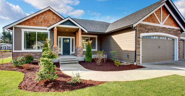 A ranch-style home features brown siding, tan and gray stones, a green front door, a walkway, and a tan garage door.