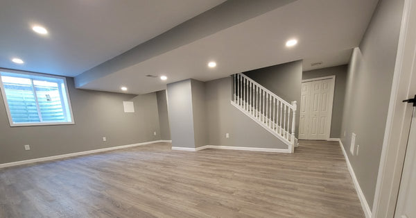 A modern, finished basement contains gray walls, a single window, and wooden floors. There are stairs leading down.