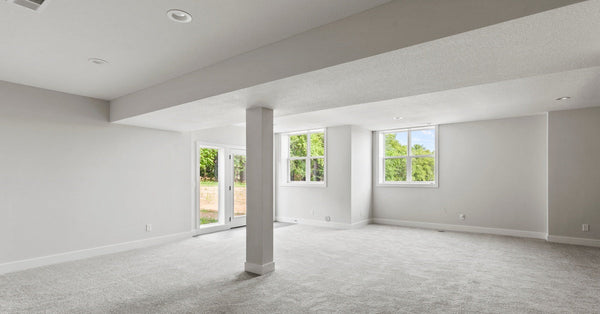 A finished basement features gray walls, a single column, gray carpet, a sliding glass door, and two windows.
