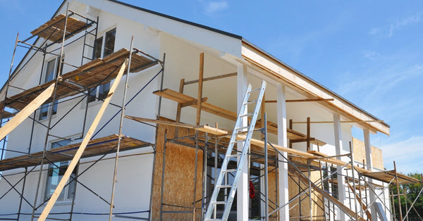 The exterior of a two-story home has scaffolding and ladders on the front and sides because of renovations.
