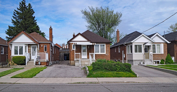 Three brick bungalow homes sit on a residential street with the blue sky shining in the background.