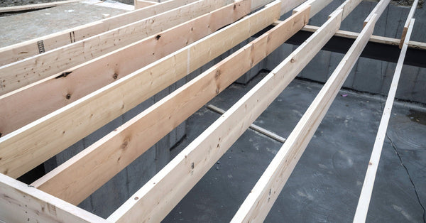 The crawl space of a home that's being built is exposed through wooden floor joists. The crawl space is concrete.