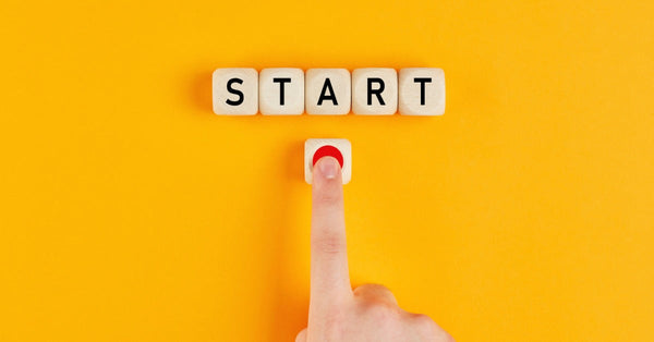 Wooden blocks line up to spell the word "START". A block with a red circle is underneath, with a finger pressing the circle.