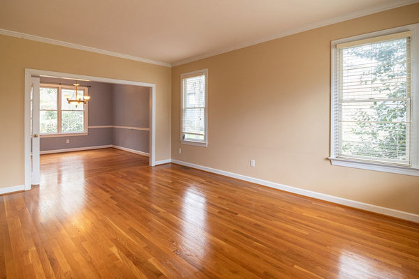 Sunlit empty living room with hardwood floors and open windows in a vacant house waiting for new occupants
